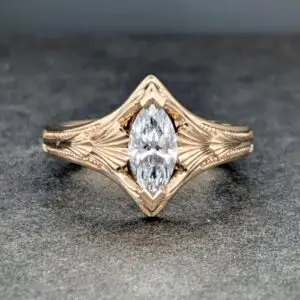 Close-up of a rose-gold ring featuring a large central diamond and carved leaf-pattern band on a dark gray surface.