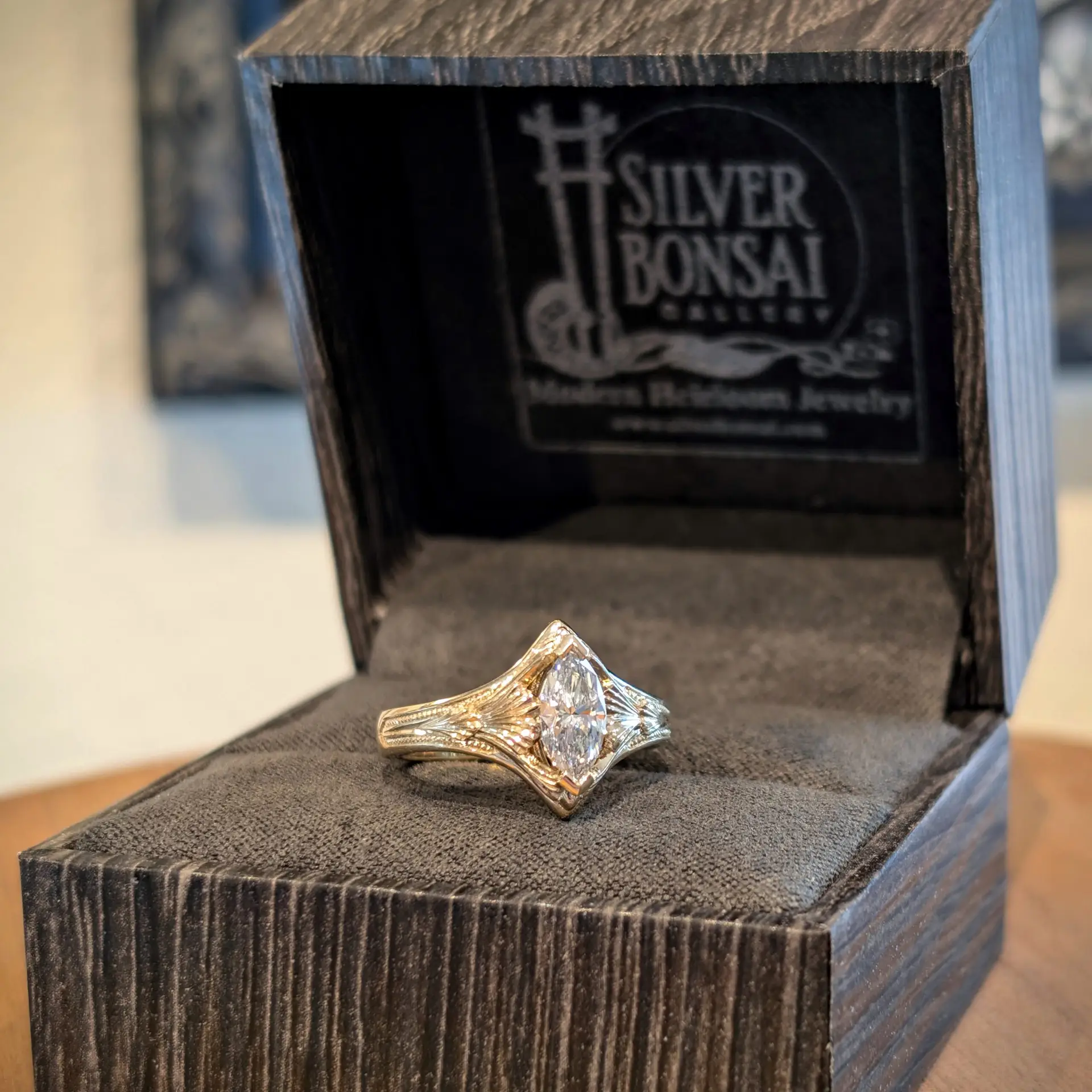 Diamond engagement ring with a large diamond sits on a black velvet interior of a wooden box, angled toward the viewer.