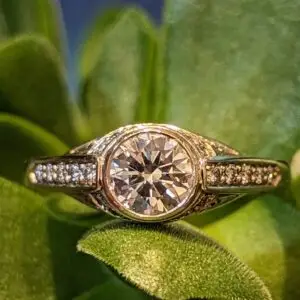 Close-up of a round-cut diamond ring with pav&eacute; band resting on bright green leaves/succulent plant.